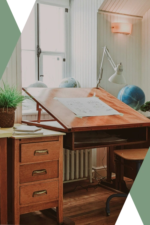 open and airy workspace featuring a drafting table, white-painted wood-paneled walls, classic wooden furniture, a window with loads of natural light, and a potted plant (featured image for "Business Execution Support" section of the Caesura Strategy "Small Business Consulting Services" page)