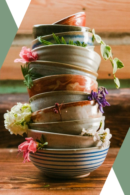 close photo of stacked handmade stoneware bowls, studded with plant sprigs, vine clippings, and fresh flowers